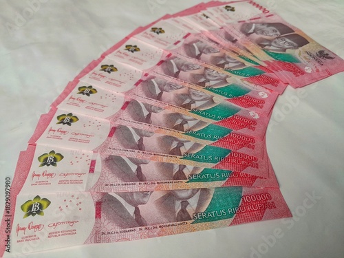 One hundred thousand rupiah notes are neatly arranged on a white table.