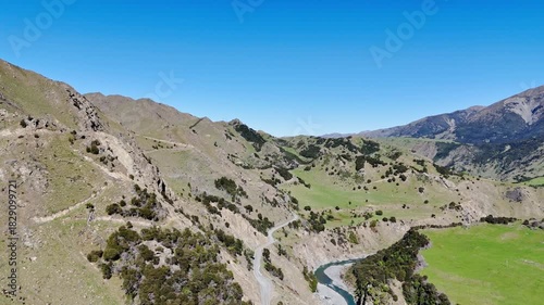 Aerial panorama showcasing a serene mountain valley with a winding river, lush green hills. 