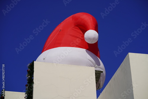 Large Inflatable Santa Hat Balloon Over Rooftop with Blue Sky Background Perfect for Holiday Decoration and Christmas Festivities
