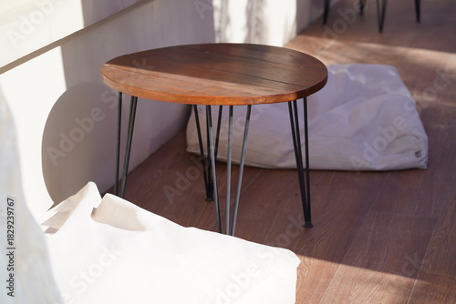 Cozy indoor seating area featuring a modern wooden table with elegant design, surrounded by soft cushions on a sunlit floor space.