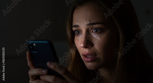 Distressed woman crying after reading bad news on her phone at night. Concept of cyberbullying, fear, and online harassment. Close-up portrait with dramatic lighting