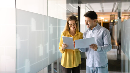 Two positive diverse business professionals discussing electronic and paper reports