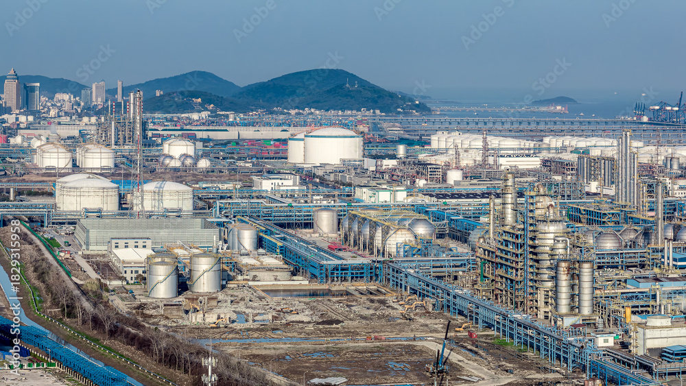 Fototapeta premium Aerial view of petrochemical industrial zone with large storage tanks and port terminals by the sea.