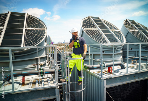 Worker conducts maintenance on rooftop cooling equipment in urban area during sunny day