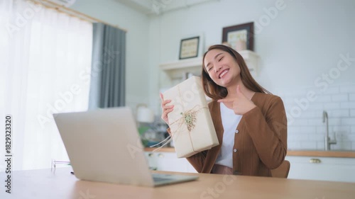 Young asian woman using computer laptop at home. Female showing gift box while on video conversation with friend. Happy birthday, Happy new year, Thanksgiving day