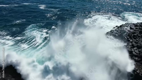 Top aerial drone view of waves crashing on rocky coastline. Blue ocean, wave and impact power. Slowly moving down. 4K.