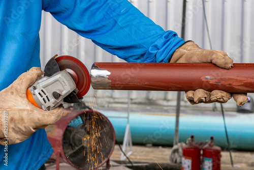 Worker using angle grinder on metal pipe