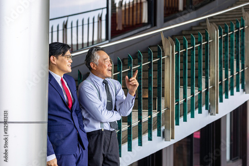 Two businessmen of different generations in formal suits networking and discussing ideas outside an office, representing workplace mentorship, collaboration, and professional growth.