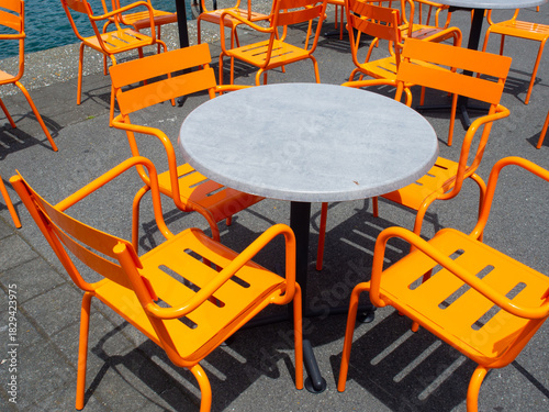 Vibrant orange chairs and table at a sunny waterfront outdoor cafe