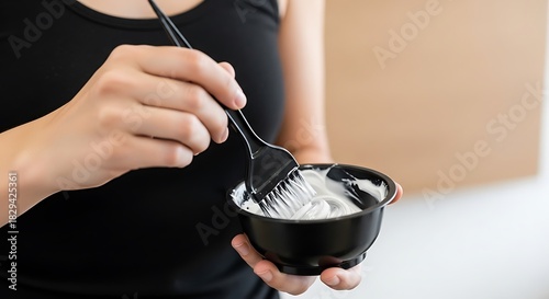 Closeup of hands mixing hair bleach or dye in a small black bowl with an applicator brush for hair coloring treatment Background image
