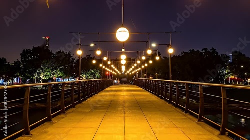 Bridge Illuminated With Warm Golden Lights At Night With A Dark Sky And Silhouetted Trees On The Sides