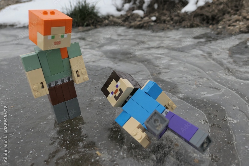 Naklejka premium LEGO Minecraft action figure of Steve laying on icy surface after fall while gliding with Alex, standing above him. Air bubbles visible under frozen ice puddle. 