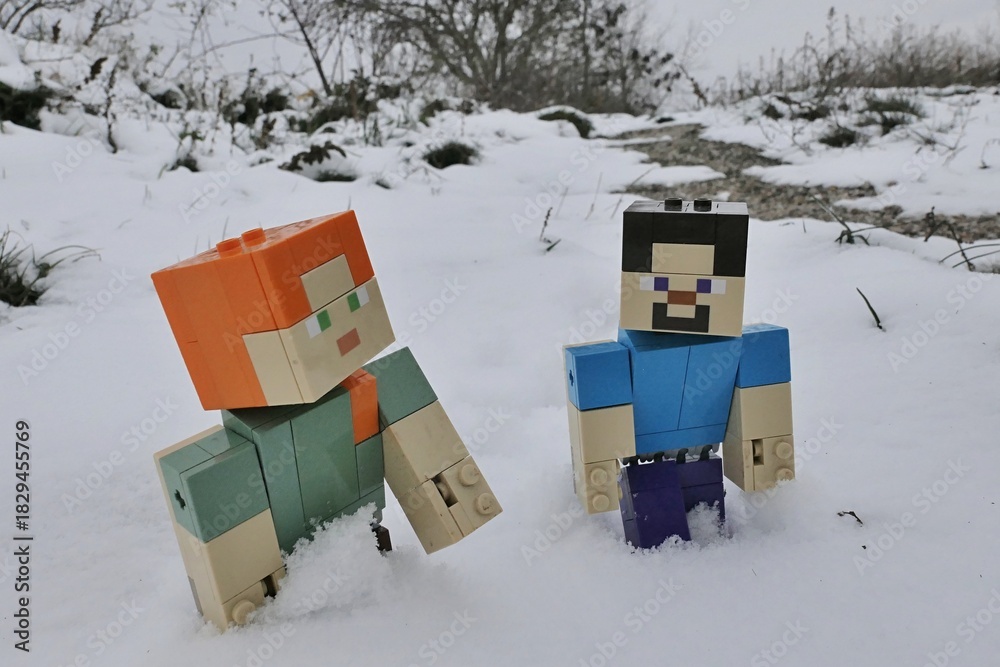 Fototapeta premium LEGO Minecraft figures of Steve and Alex trudging in deep snow on edge of winter agricultura field during cloudy winter day.
