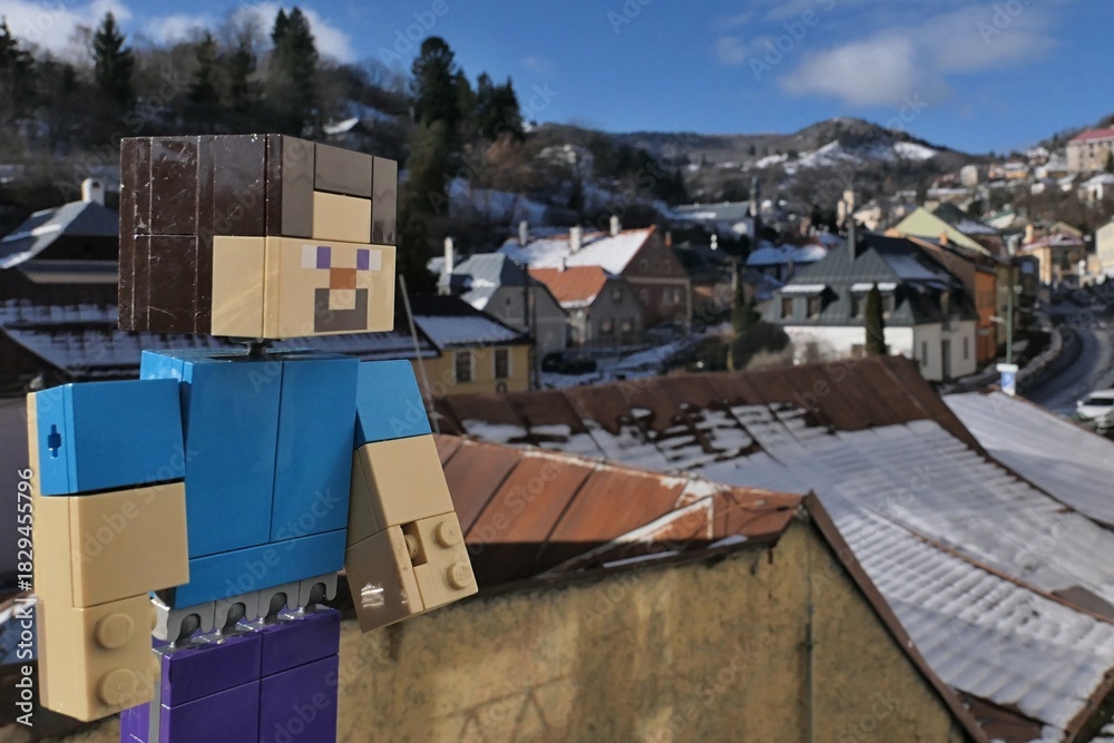 Naklejka premium LEGO Minecraft smiling action figure of main character Steve, enjoying view snow covered roofs in UNESCO mining town of Banska Stiavnica from Zvonova street during sunny winter day.