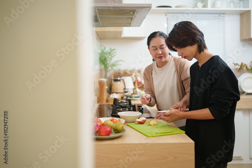 Asian grandmother teaching the Chinese boy how to cut fruits at the counter, sharing a soft moment.