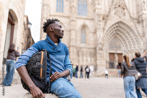 African American man with backpack sitting, resting during his trip, exploring Barcelona's Gothic Quarter