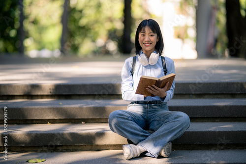 Asian student reading book on college campus stairs