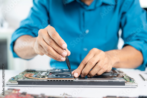 Technician repairing laptop computer using screwdriver on motherboard
