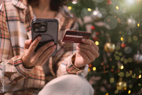 woman using Mobile holiday shopping payment person holding smartphone and credit card to complete secure online transactions during festive Christmas season