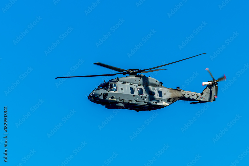 Fototapeta premium Military helicopter in the air on blue sky background. Gray patrol helix close up. Naval helicopter vehicle flying.
