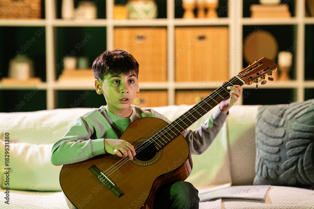 Obraz premium Young boy learning to play classical acoustic guitar at home