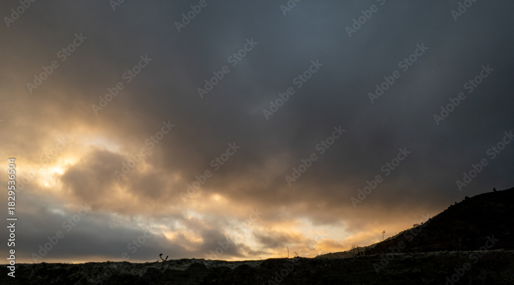 Fototapeta premium Dark dramatic sky with glowing clouds over silhouette landscape