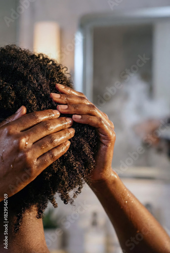 Back view of a Black woman performing a wash day routine on natural afro hair, massaging scalp with shampoo or conditioner, symbolizing self care and beauty rituals
