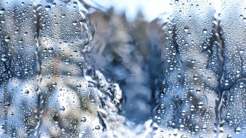 Macro shot of water condensation droplets streaming down a cold glass window pane blurring the icy snowy forest background environment warmth, close-up, atmosphere