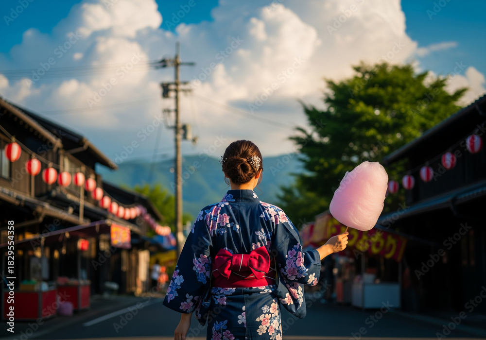 Fototapeta premium 綿アメを持ち、古い町並みを歩く浴衣姿の女性の後ろ姿