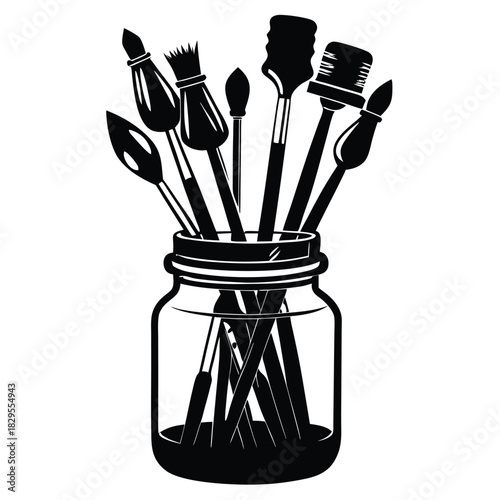 Assorted paintbrushes are arranged artfully within a glass mason jar in silhouette