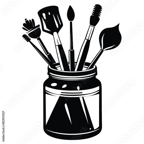 Various black paintbrushes stand creatively inside of a clear glass jar in monochrome style