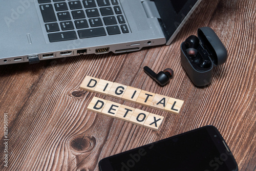 Flat lay composition featuring a Digital Detox sign surrounded by a smartphone, headphones, and laptop. Concept of unplugging, reducing screen time, and mental health awareness
