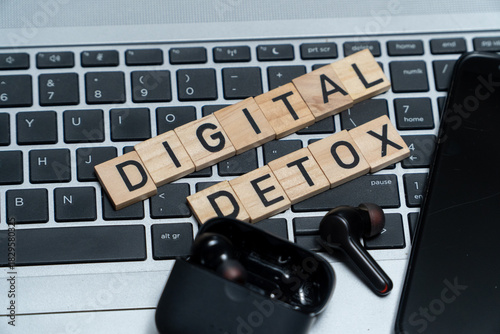 Flat lay composition featuring a Digital Detox sign surrounded by a smartphone, headphones, and laptop. Concept of unplugging, reducing screen time, and mental health awareness