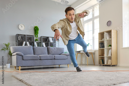 Foto Clumsy man tripping over cord at home, unsafe falling as domestic hazard in living room
