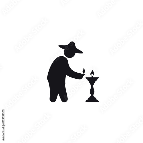 Silhouette of a person lighting a candle on a stand.