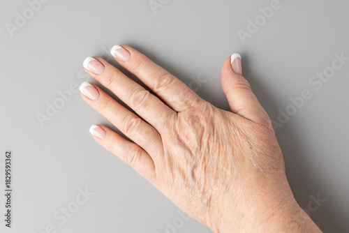 Slika na platnu Aging hand of adult 70 year old woman with age spots, deep wrinkles on skin and french manicure nails