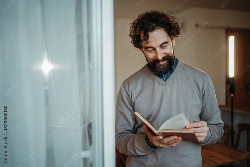 Fototapeta premium Bearded man reading old book feeling relaxed indoors