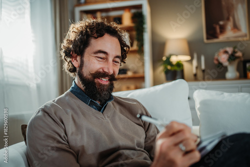 Happy man writing in journal relaxing at home