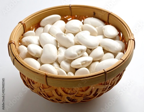 White lima beans overflowing in a small, round woven basket, casting a shadow on a white surface
