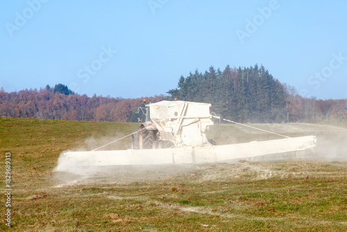 Chemical fertilisation of farm pasture with tractor pulling a chemical drop boom spreader, winter sunset, mechanisation
