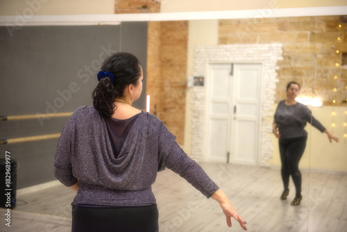A confident plus-size woman practices expressive dance movements in a studio, embracing body positivity and freedom while training in front of large mirrors.