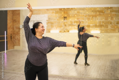 A confident plus-size woman practices expressive dance movements in a studio, embracing body positivity and freedom while training in front of large mirrors.