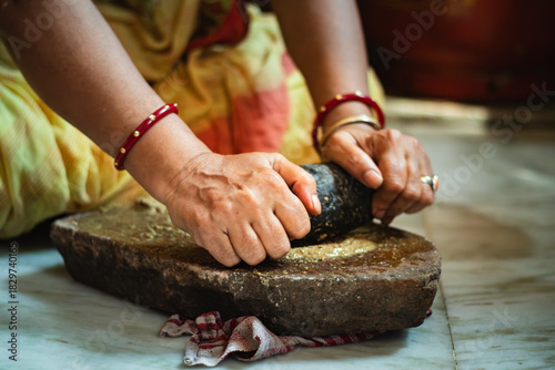 Quadro su tela Indian Woman Grinding Spices on Traditional sil batta or Stone Grinder in Kitchen
