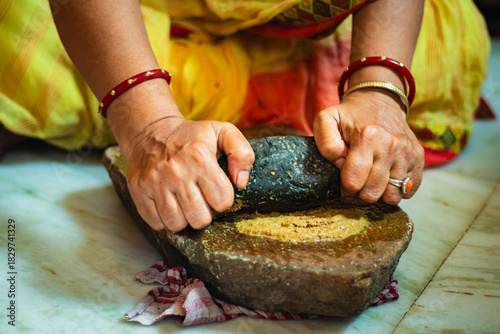 Foto Indian Woman Grinding Spices on Traditional sil batta or Stone Grinder in Kitchen