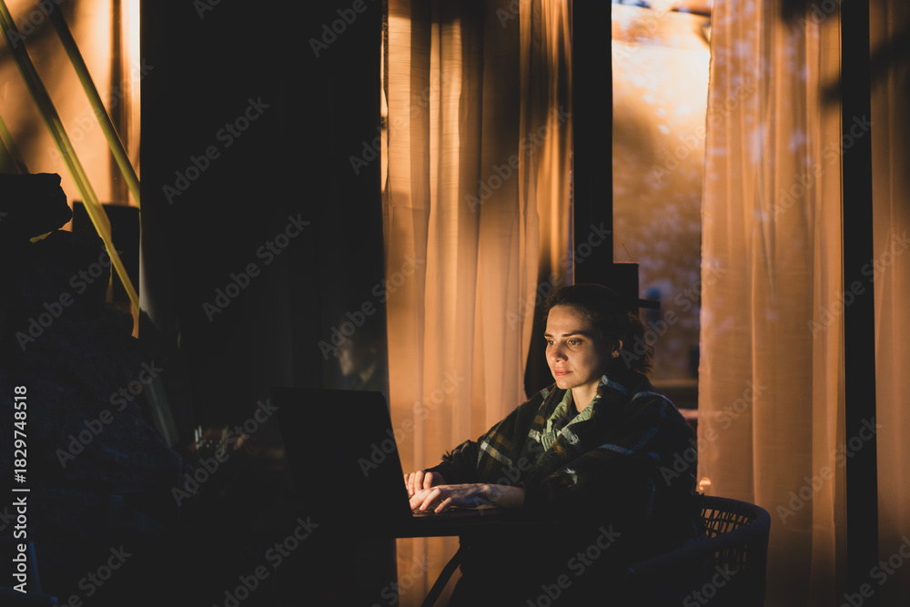 Obraz premium Young hysster woman working on a laptop in the evening on the open terrace of her country house