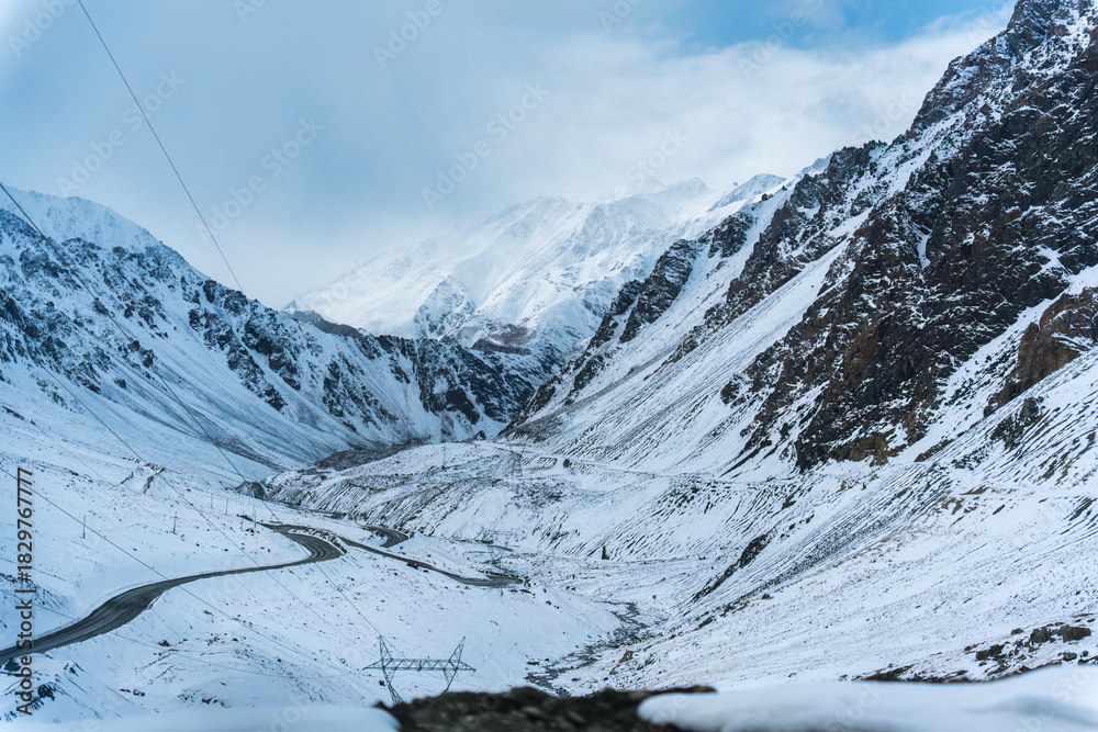 Obraz premium Scenic snowy valley with mountain pass, curving road, and winter landscape surrounded by steep slope