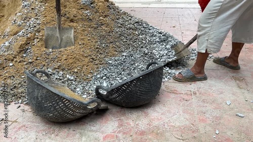 Worker Using Shovel to Scoop Sand and rock into Basket