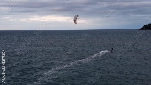 A kitesurfer rides parallel to the coastline, creating a lively rhythm against the shifting textures of the sea.