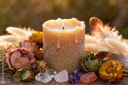 Beeswax candle surrounded by dried flowers and colorful crystals  
