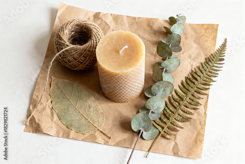 Beeswax candle with twine and leaves on brown paper background  